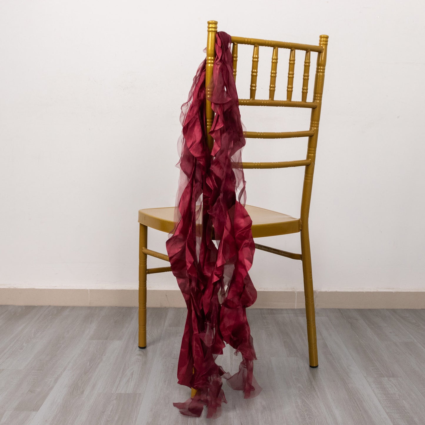 Burgundy curly chiffon satin chair sashes draped over a gold chair.