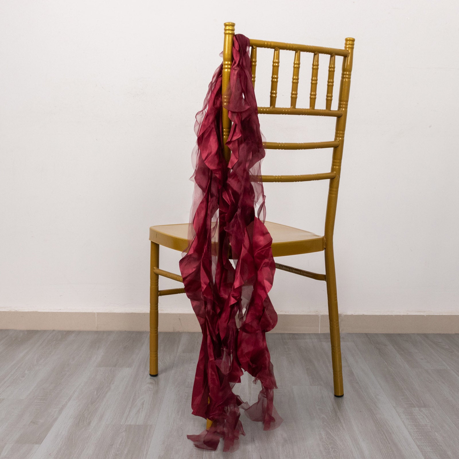 Burgundy curly chiffon satin chair sashes draped over a gold chair.