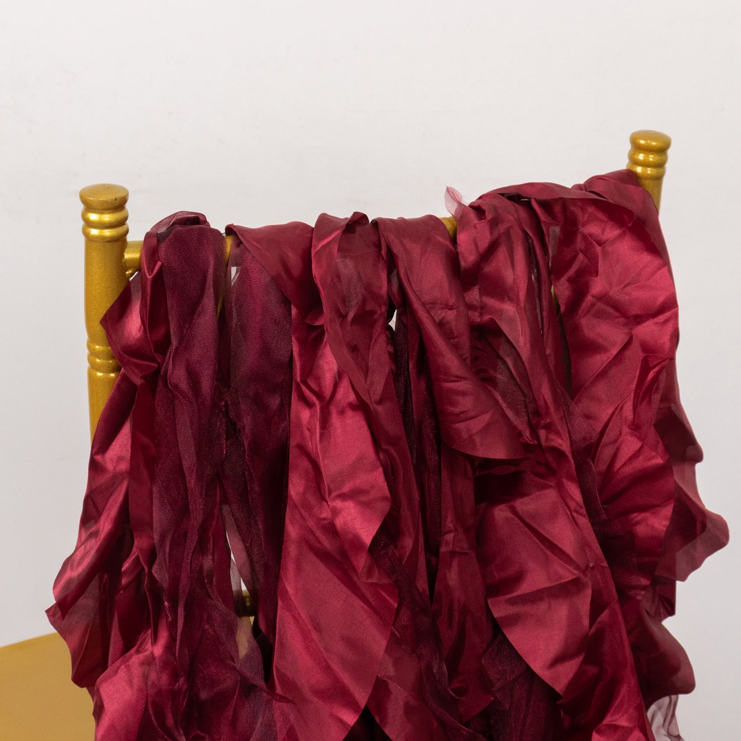 Burgundy chiffon satin chair sashes draped over a golden chair.