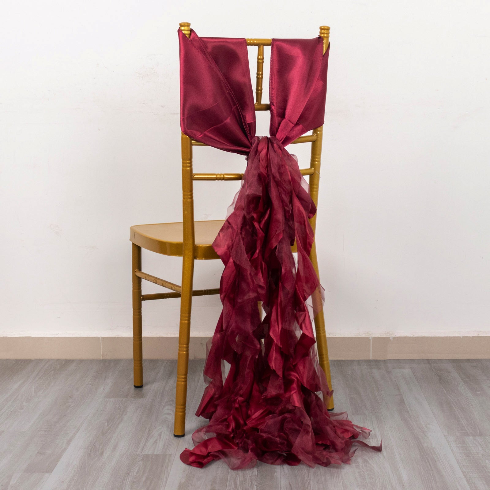 Burgundy curly chiffon satin chair sash tied on a gold chair.