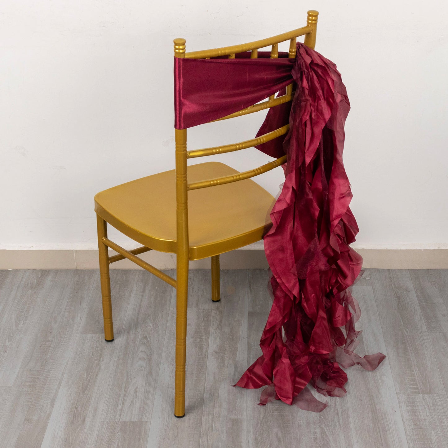 Burgundy chiffon satin chair sash draped on a gold chair.