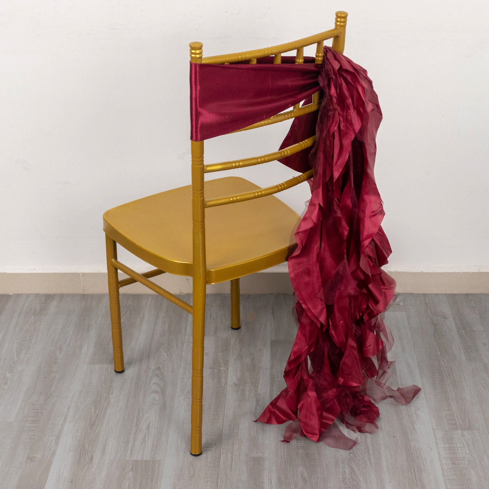Burgundy chiffon satin chair sash draped on a gold chair.