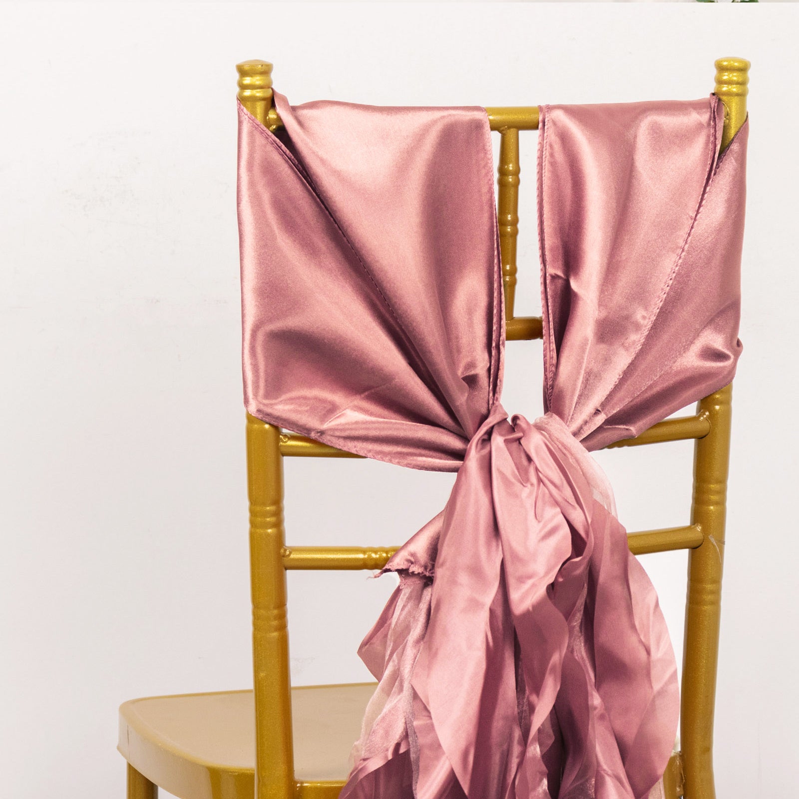 Cinnamon rose satin chair sash tied on a gold chair.
