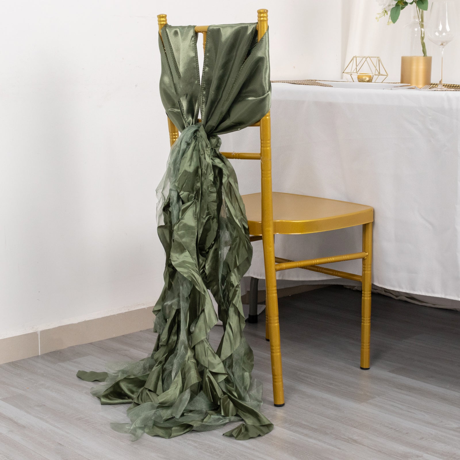 Dusty sage green curly chiffon satin chair sash on a yellow chair.