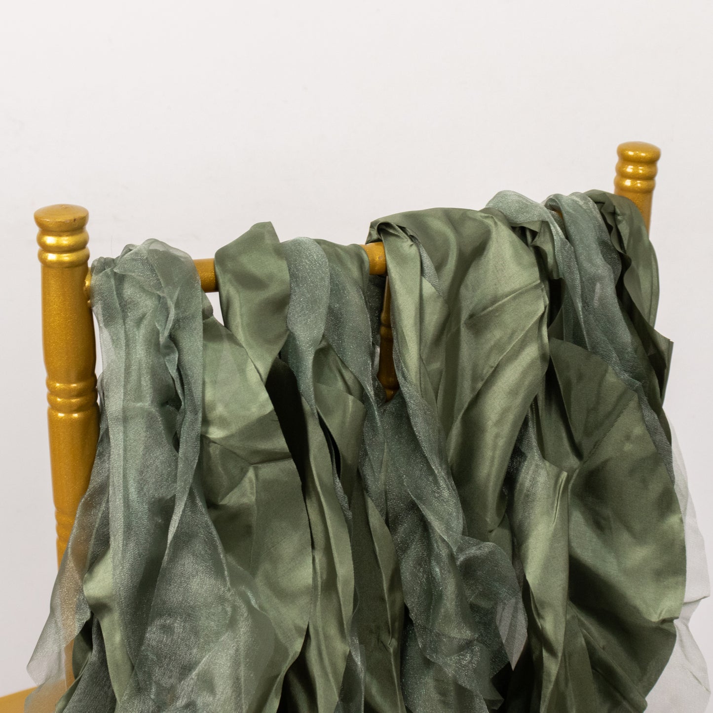 Dusty sage green chiffon satin chair sashes displayed on a golden chair.