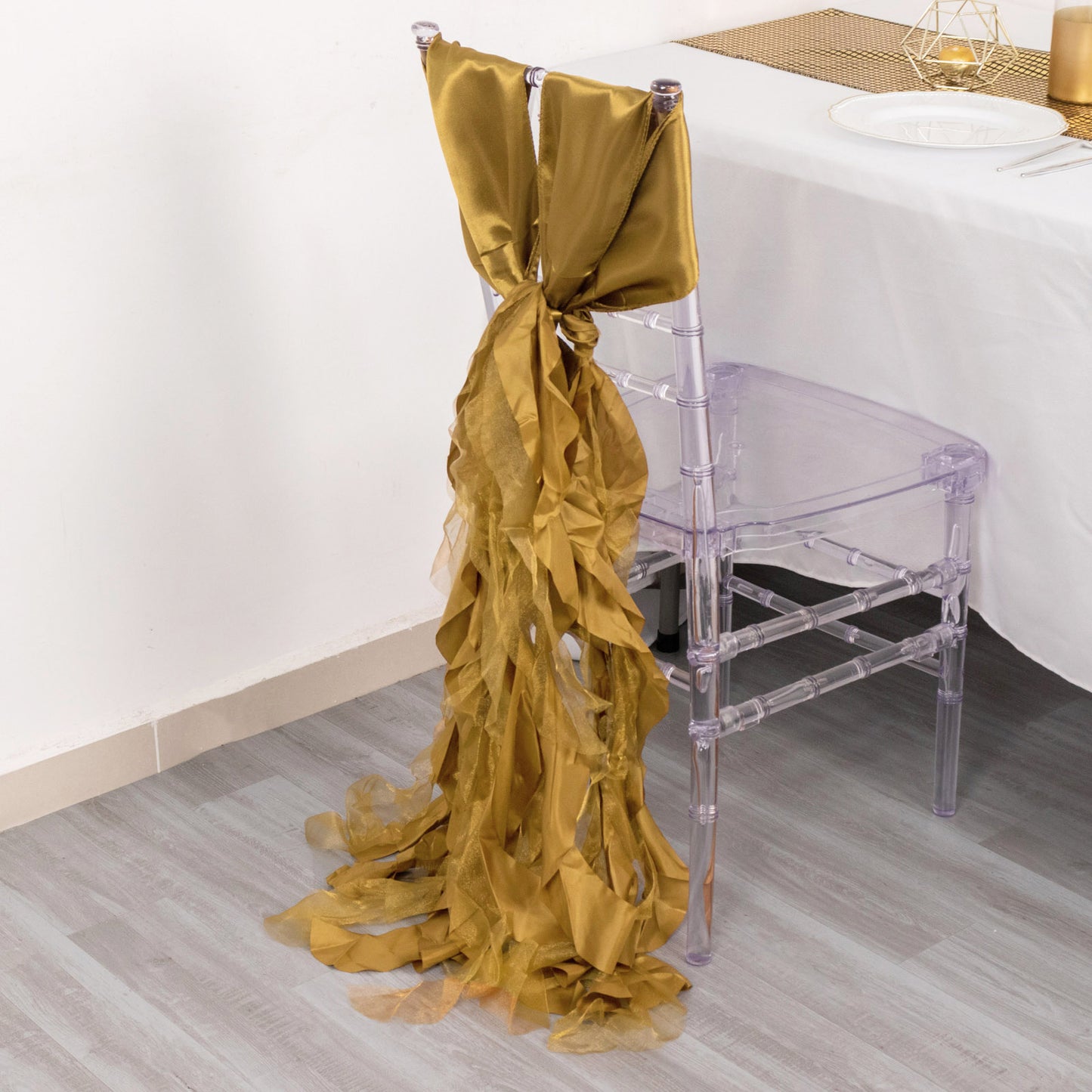 Gold curly willow chiffon satin chair sash draped elegantly on a clear chair.