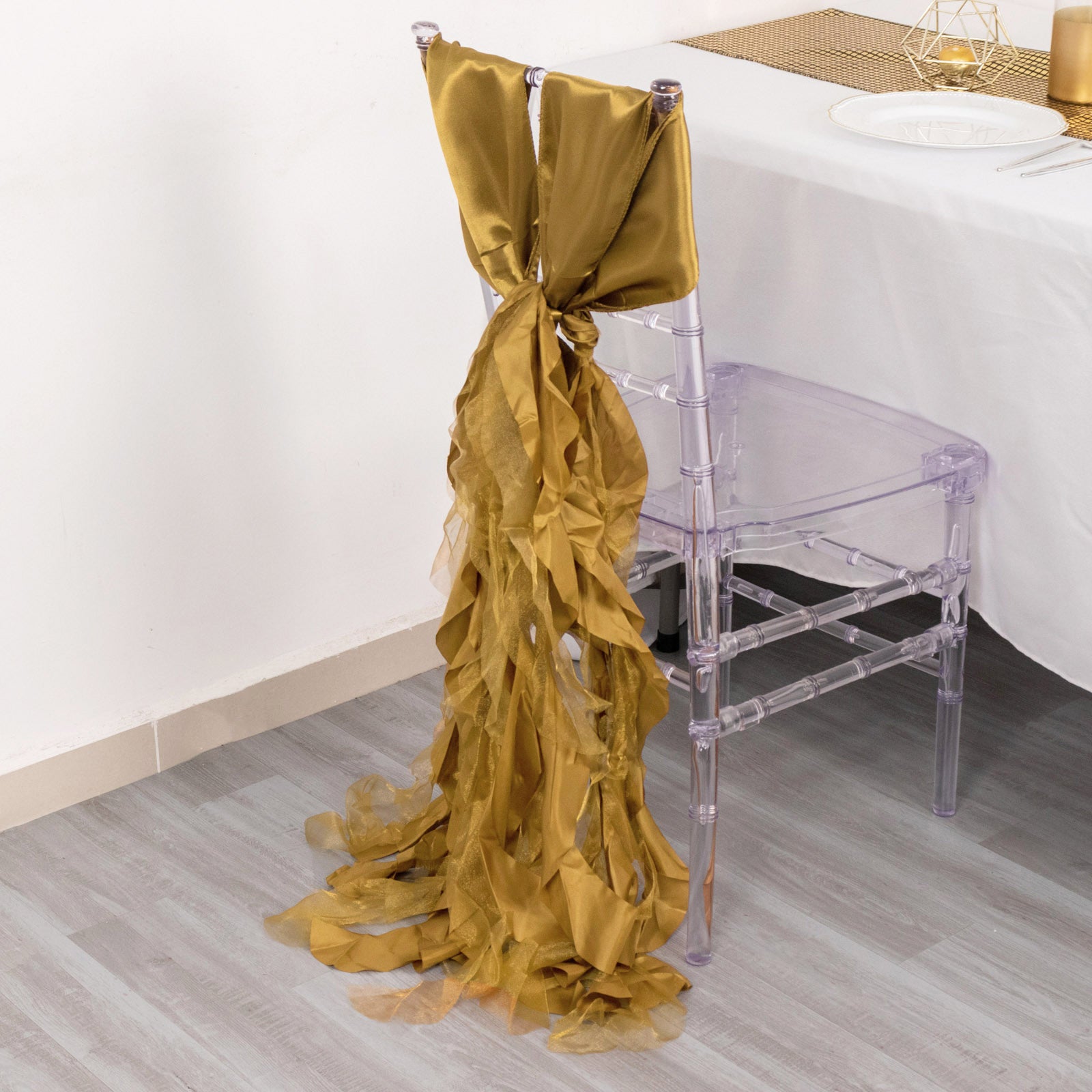 Gold curly willow chiffon satin chair sash draped elegantly on a clear chair.