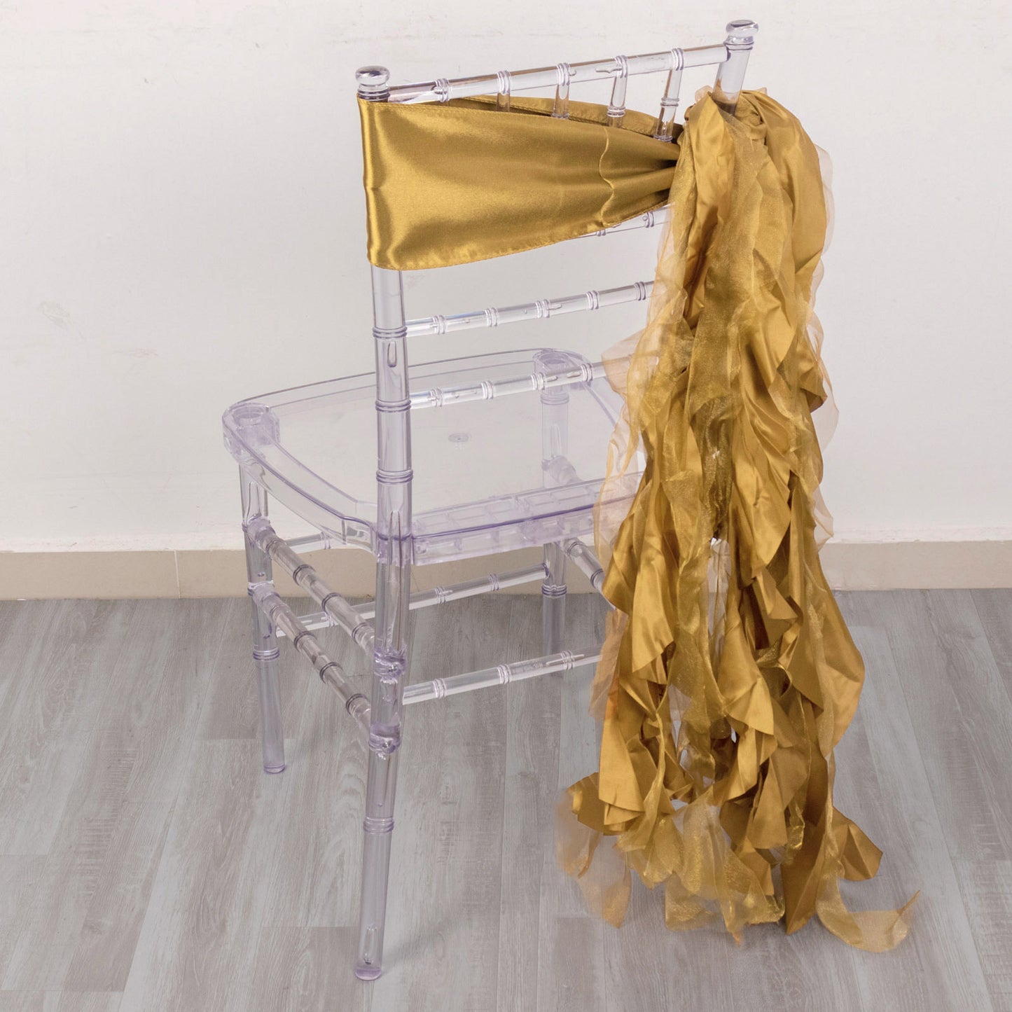 Gold chiffon satin chair sash draped over a clear chair.
