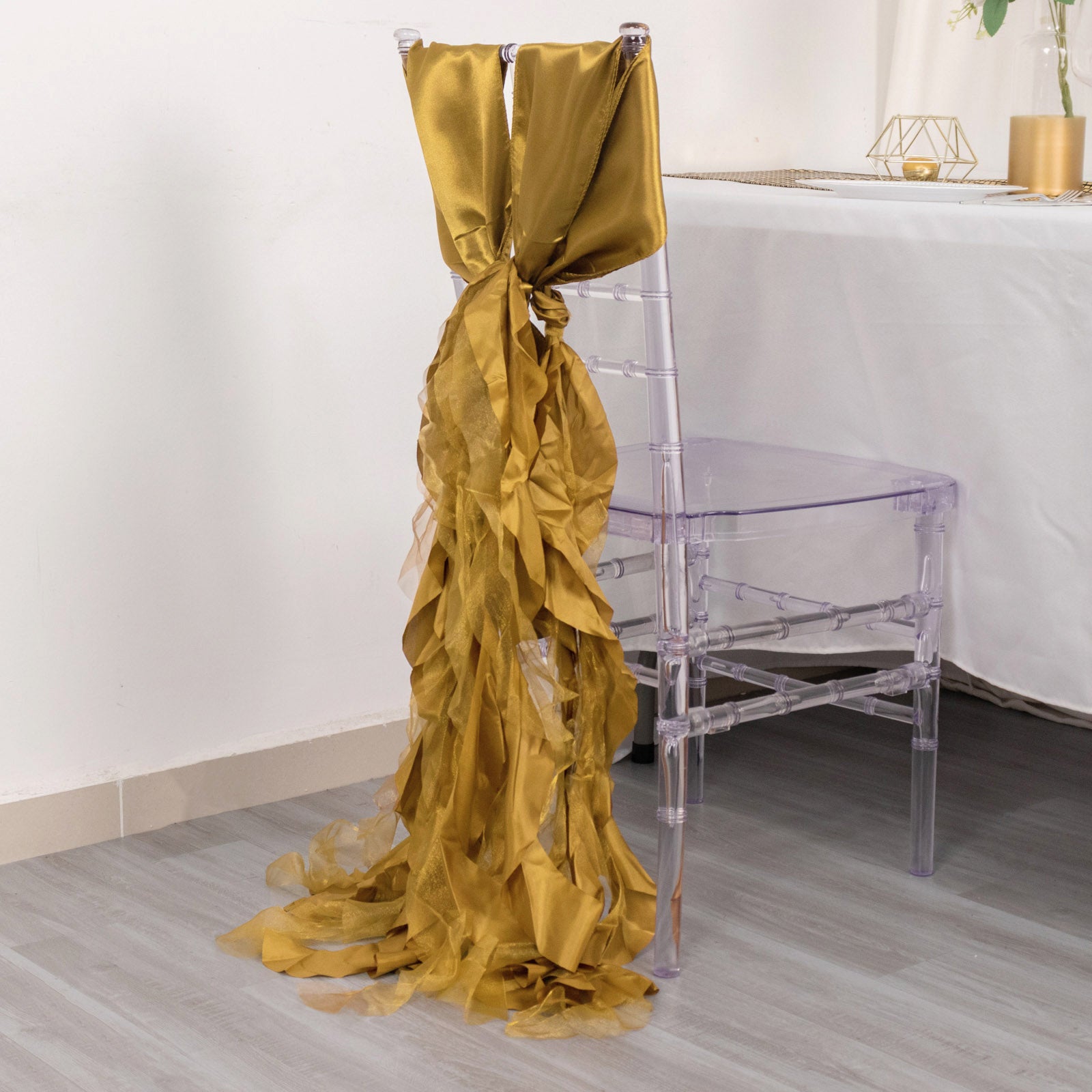 Gold curly willow chiffon satin chair sash draped on a clear chair.