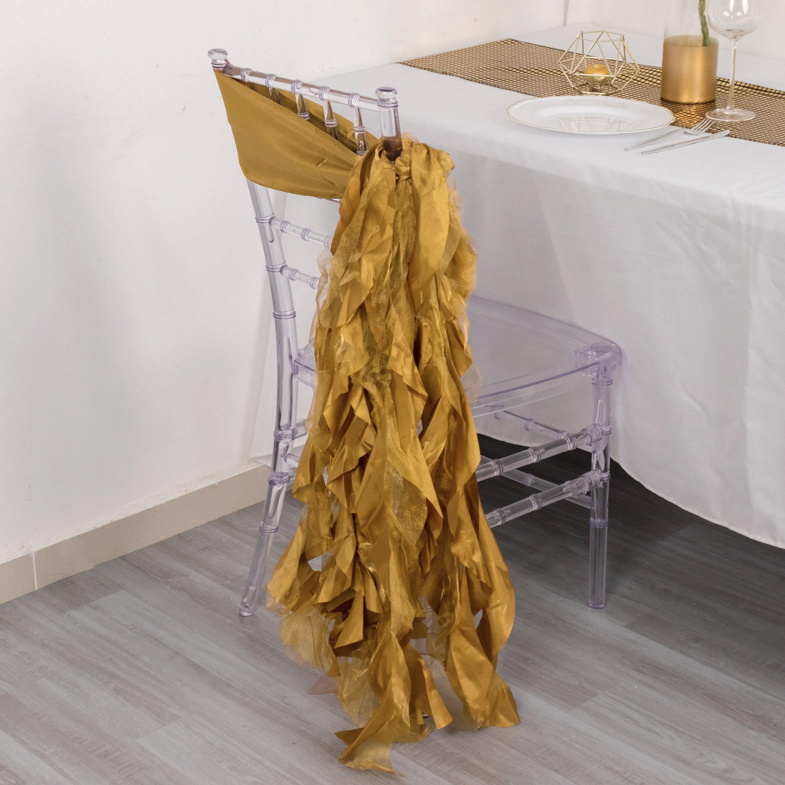 Gold curly willow chiffon satin chair sashes draped on a clear chair.