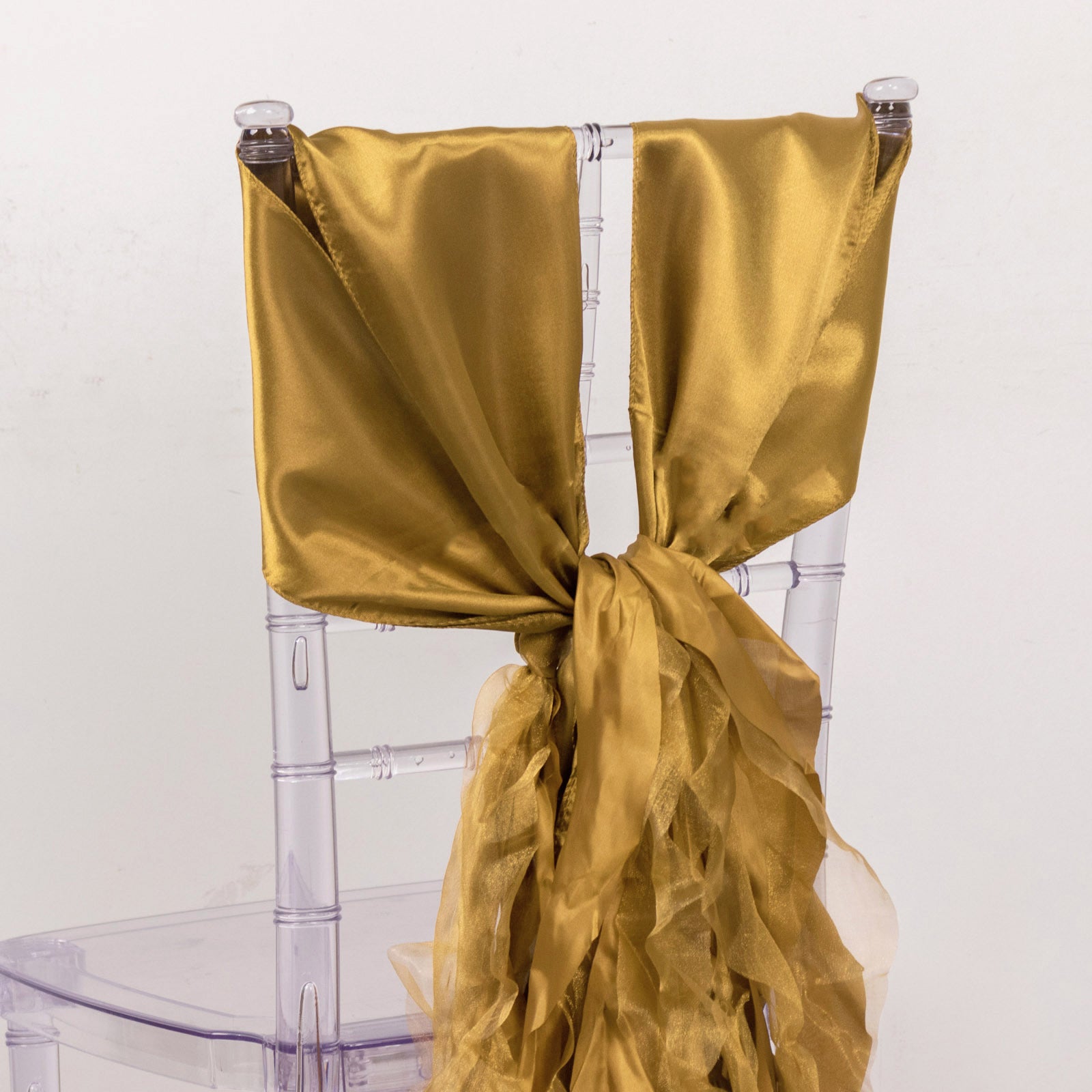 Gold curly willow chiffon satin chair sashes tied on a clear chair.