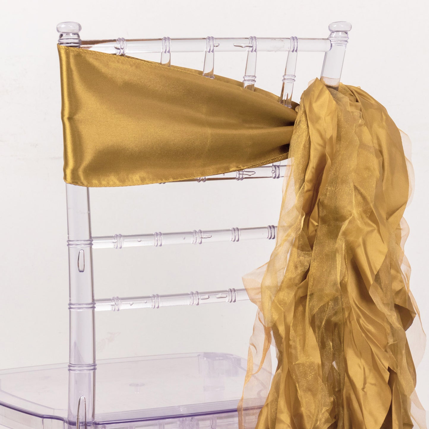 Gold curly willow chiffon satin chair sash on a clear chair.