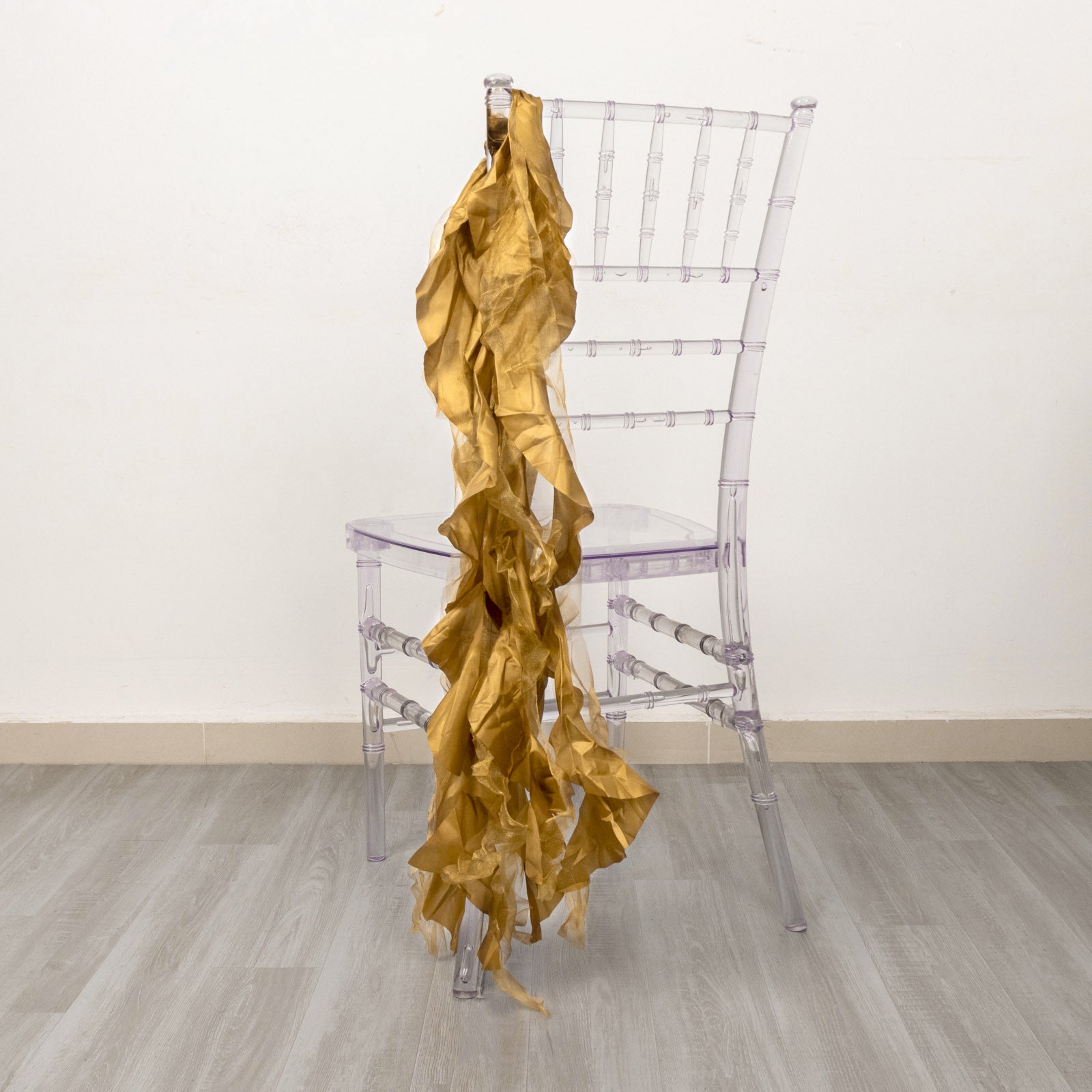 Gold curly chiffon satin chair sashes draped over a clear chair.