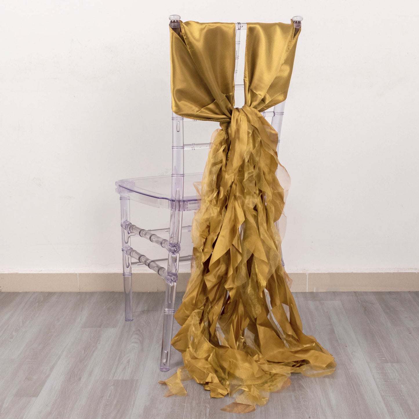 Gold curly chiffon satin chair sash elegantly draped on a clear plastic chair.