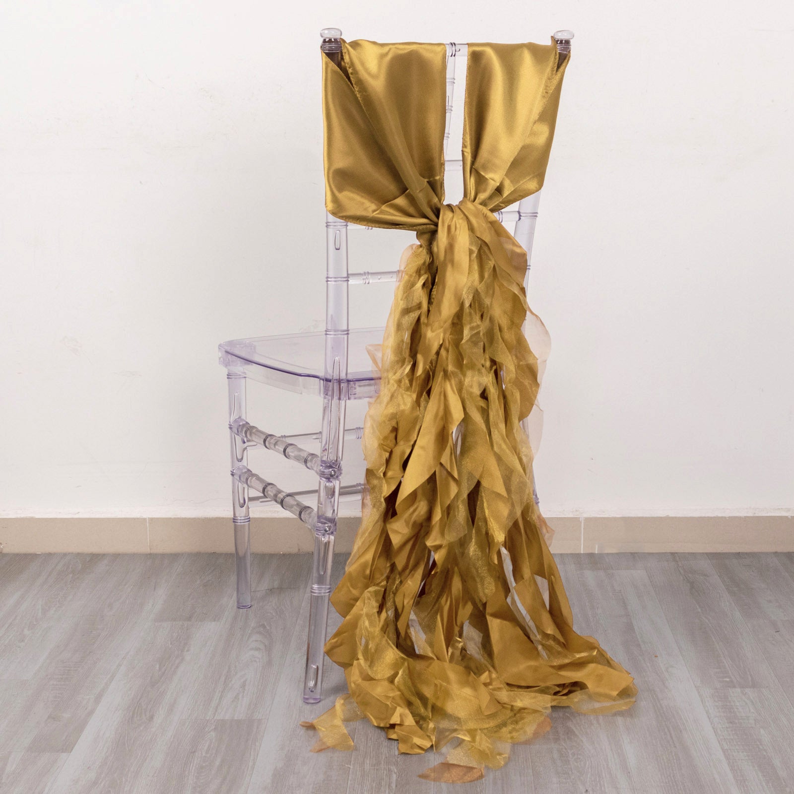 Gold curly chiffon satin chair sash elegantly draped on a clear plastic chair.