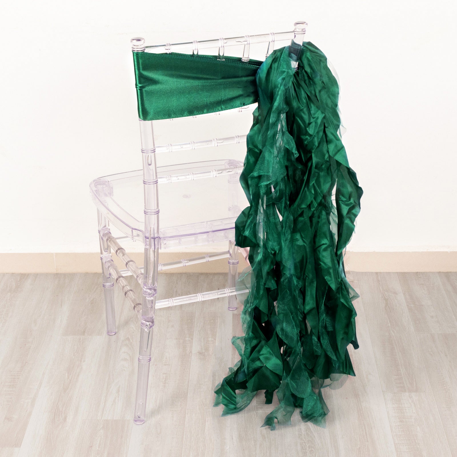 Emerald green curly chiffon satin chair sashes on a clear chair.
