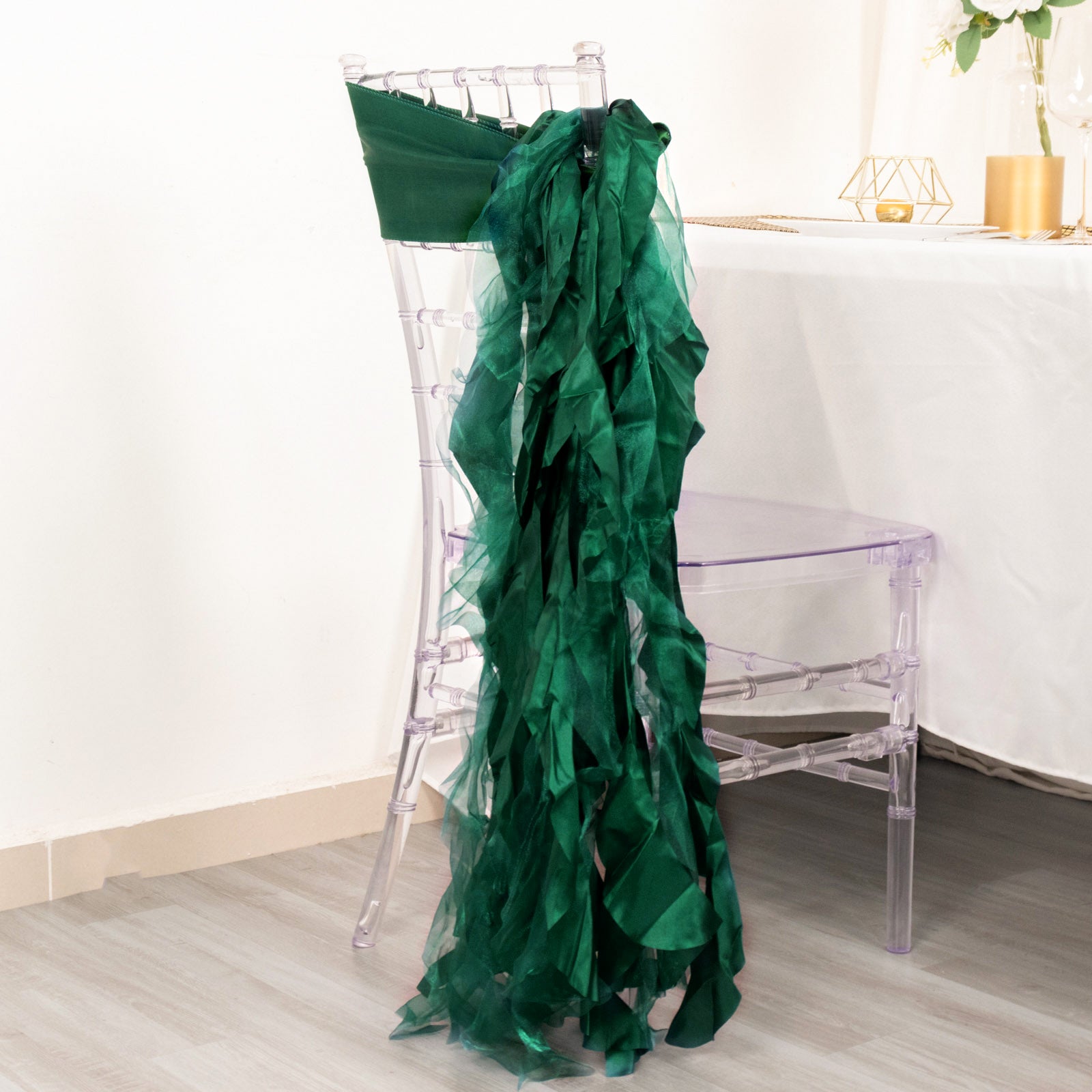 Emerald green curly chiffon satin chair sash draped on a clear chair.
