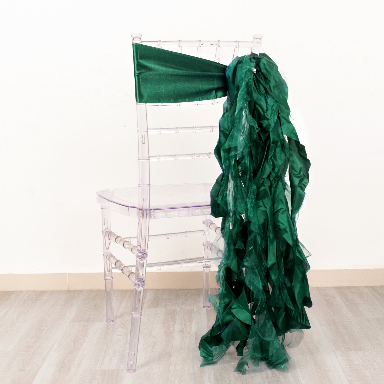 Emerald green curly chiffon satin chair sashes on a transparent chair.