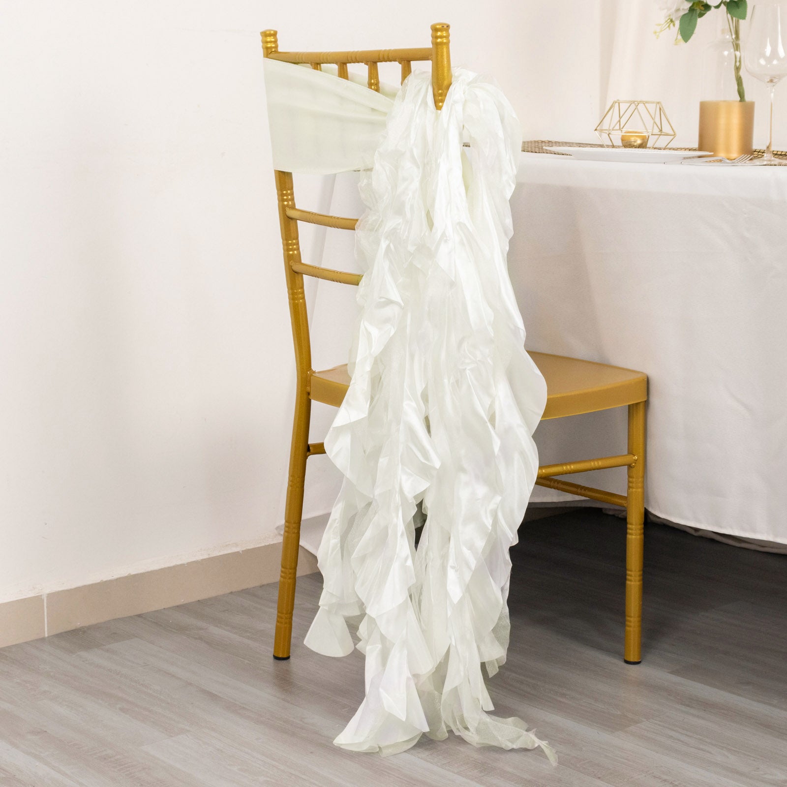 Ivory curly chiffon satin chair sash draped on a gold chiavari chair.