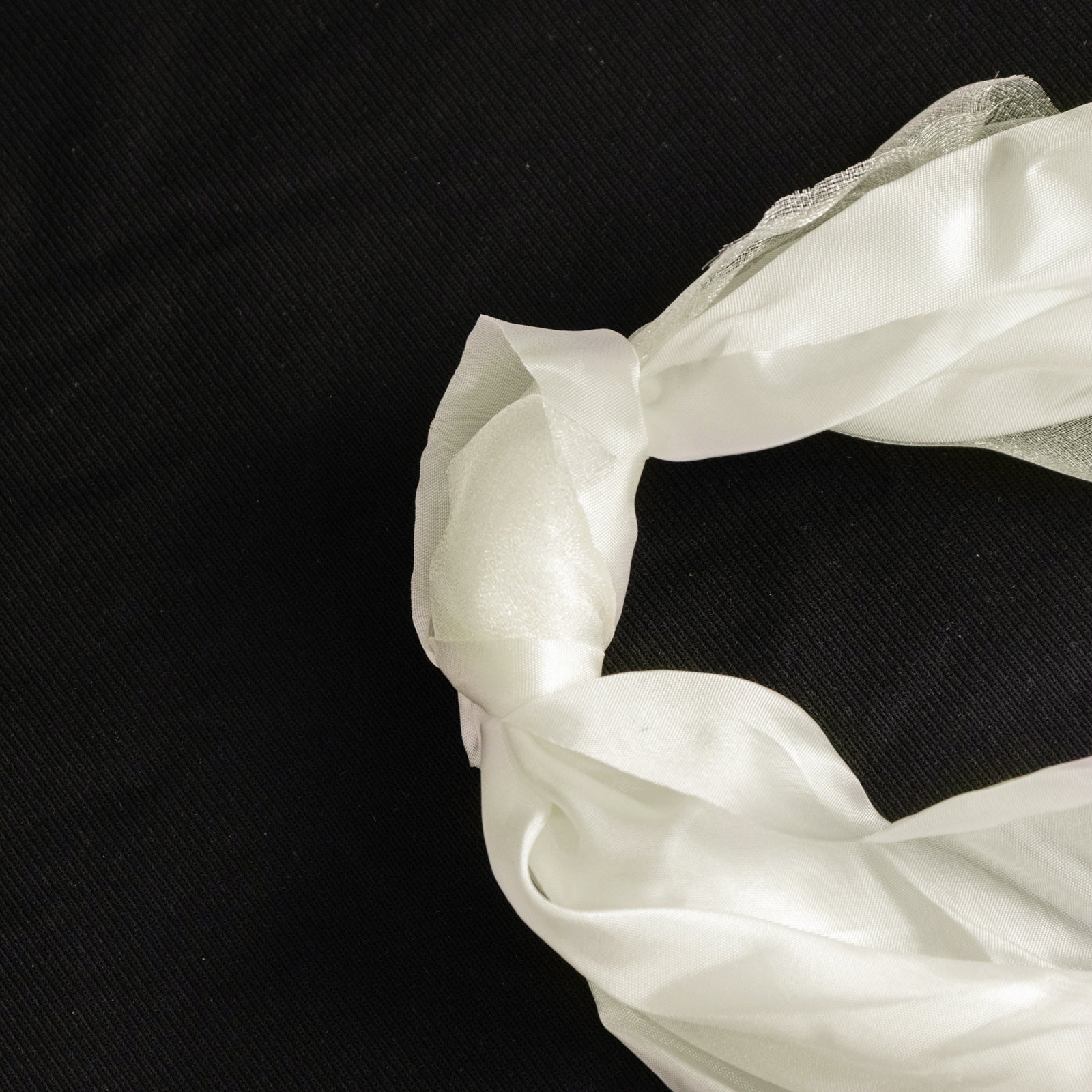 Ivory chiffon satin chair sash tied in a knot on a black background.
