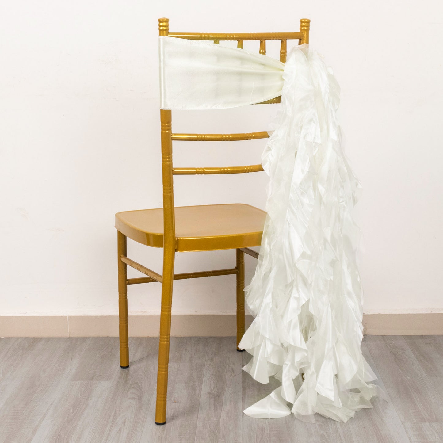 Ivory curly chiffon satin chair sash draped on a gold chiavari chair.