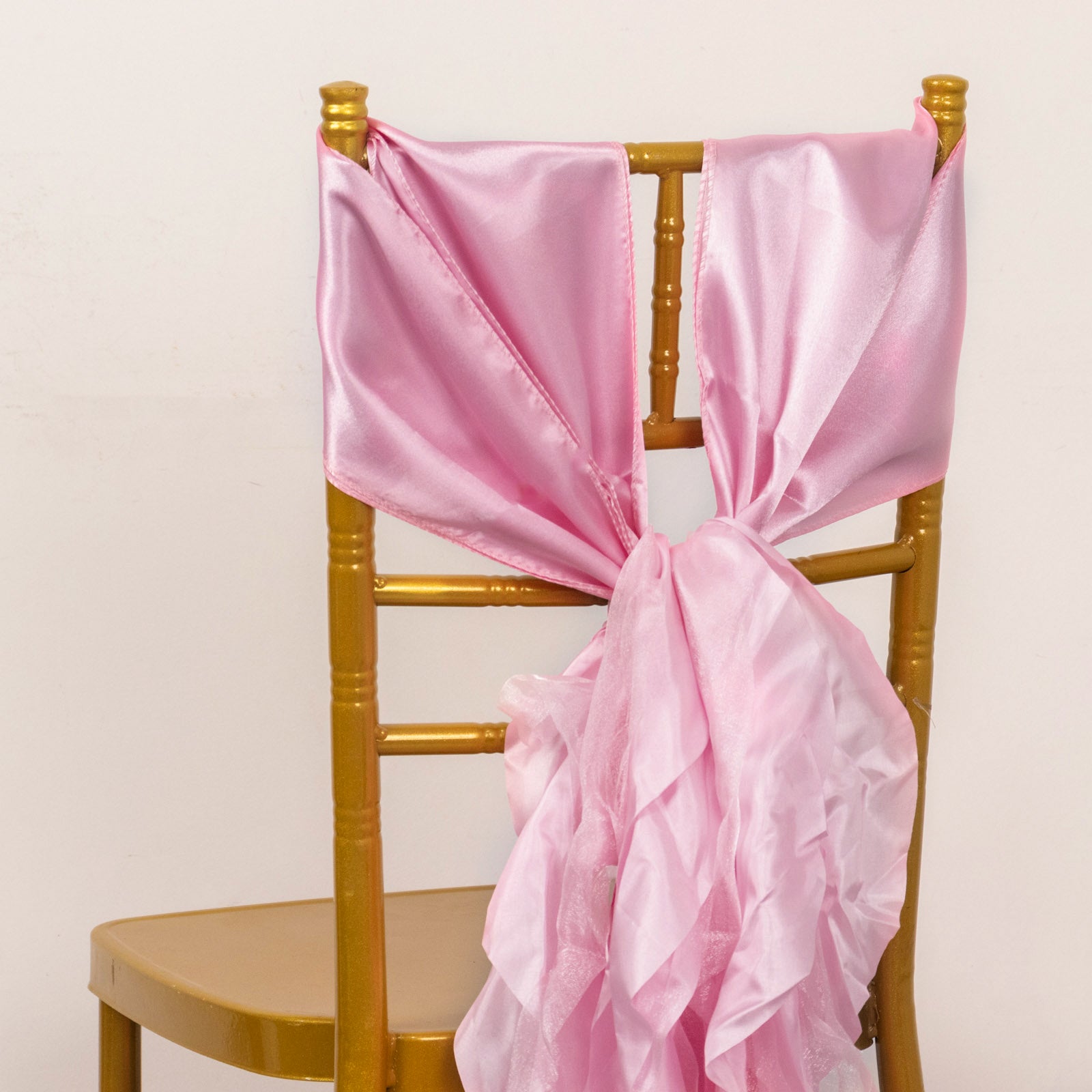 Pink chiffon satin chair sash tied on a gold chair.