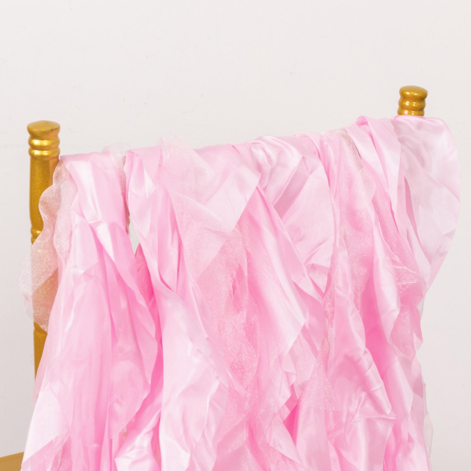Pink chiffon satin chair sashes draped over a gold chair.