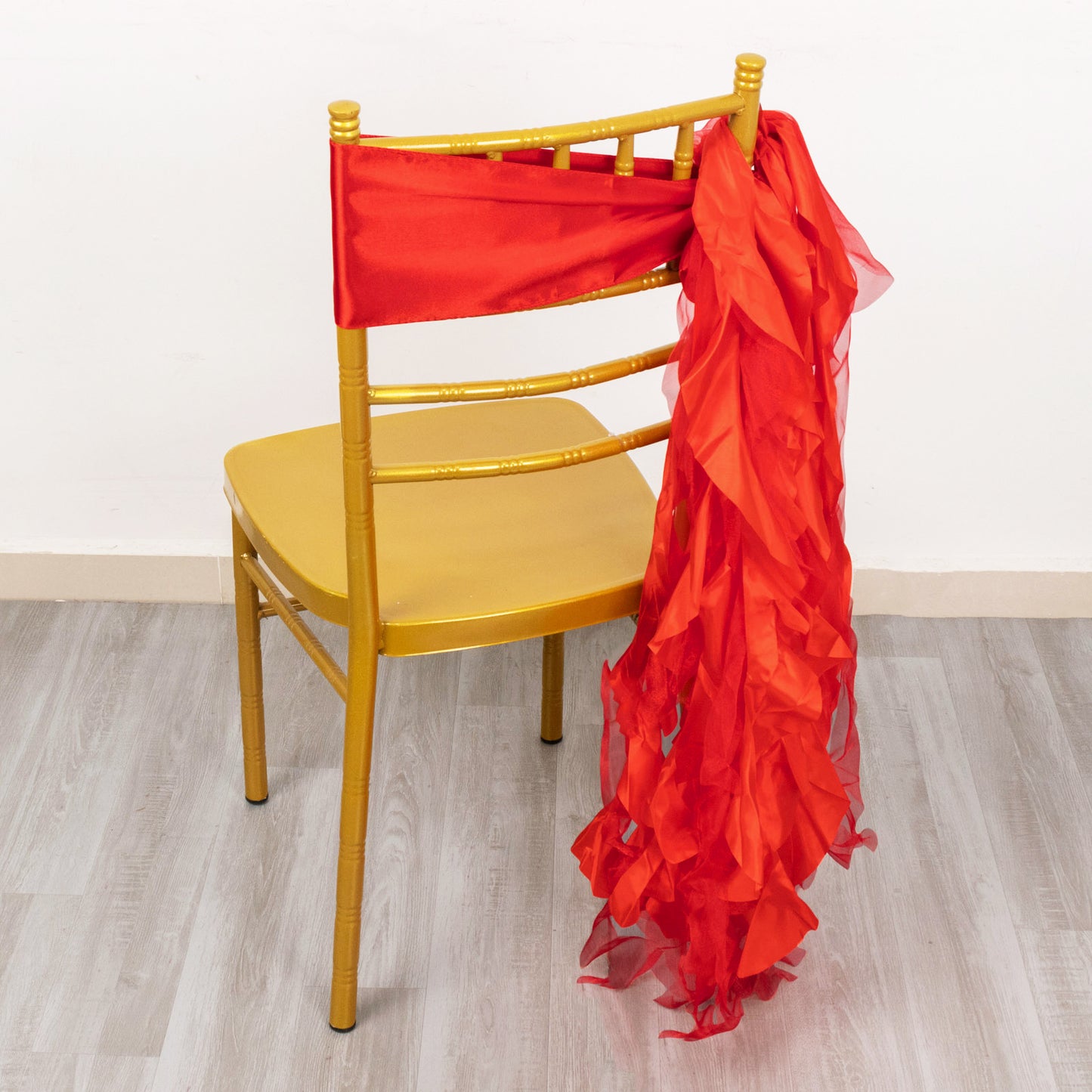 Red curly chiffon satin chair sash draped on a gold chair.