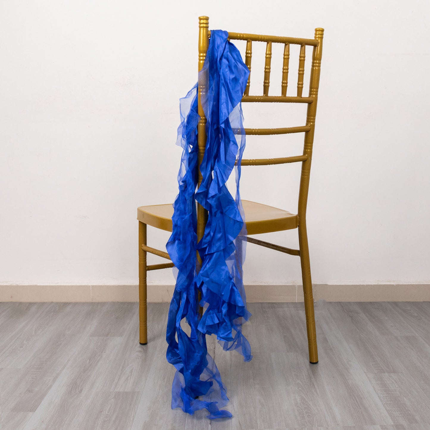 Royal blue curly chiffon satin chair sashes draped on a golden chair.