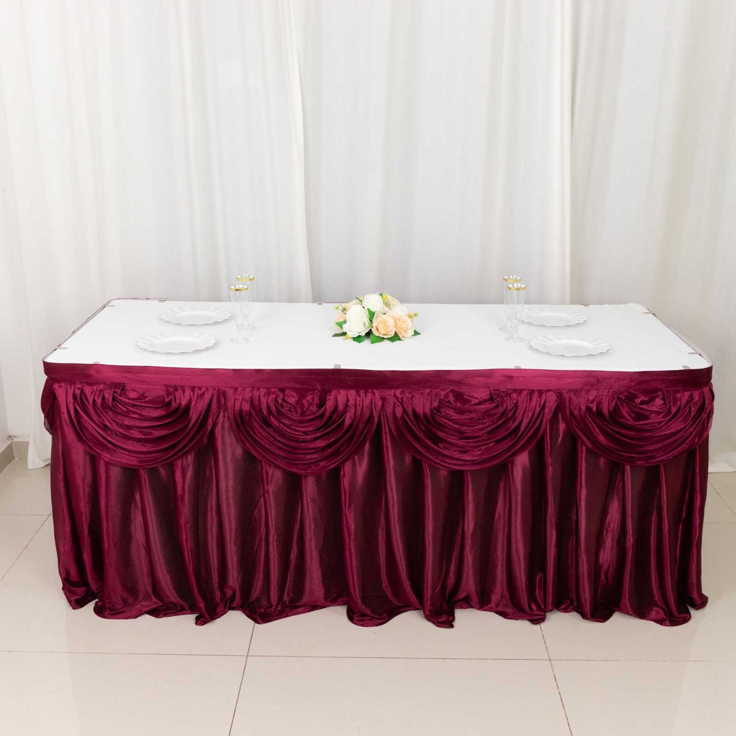 14ft burgundy pleated satin double drape table skirt on a table.