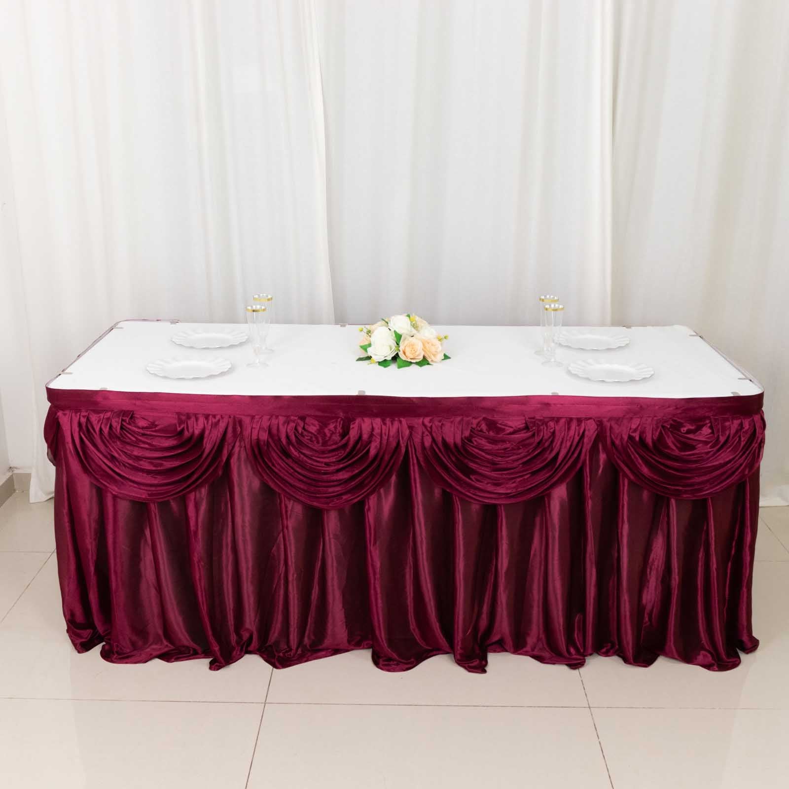 14ft burgundy pleated satin double drape table skirt on a table.