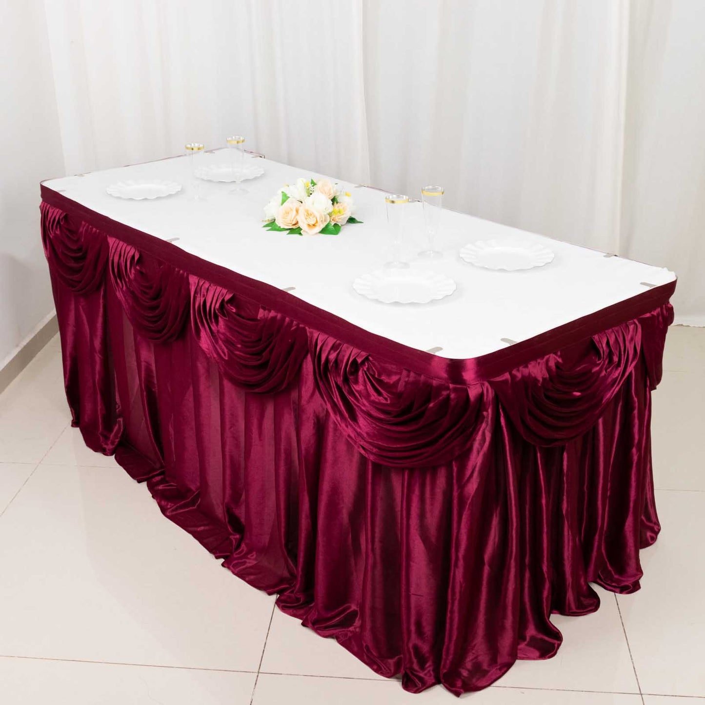 Burgundy pleated satin table skirt draped elegantly on a table.