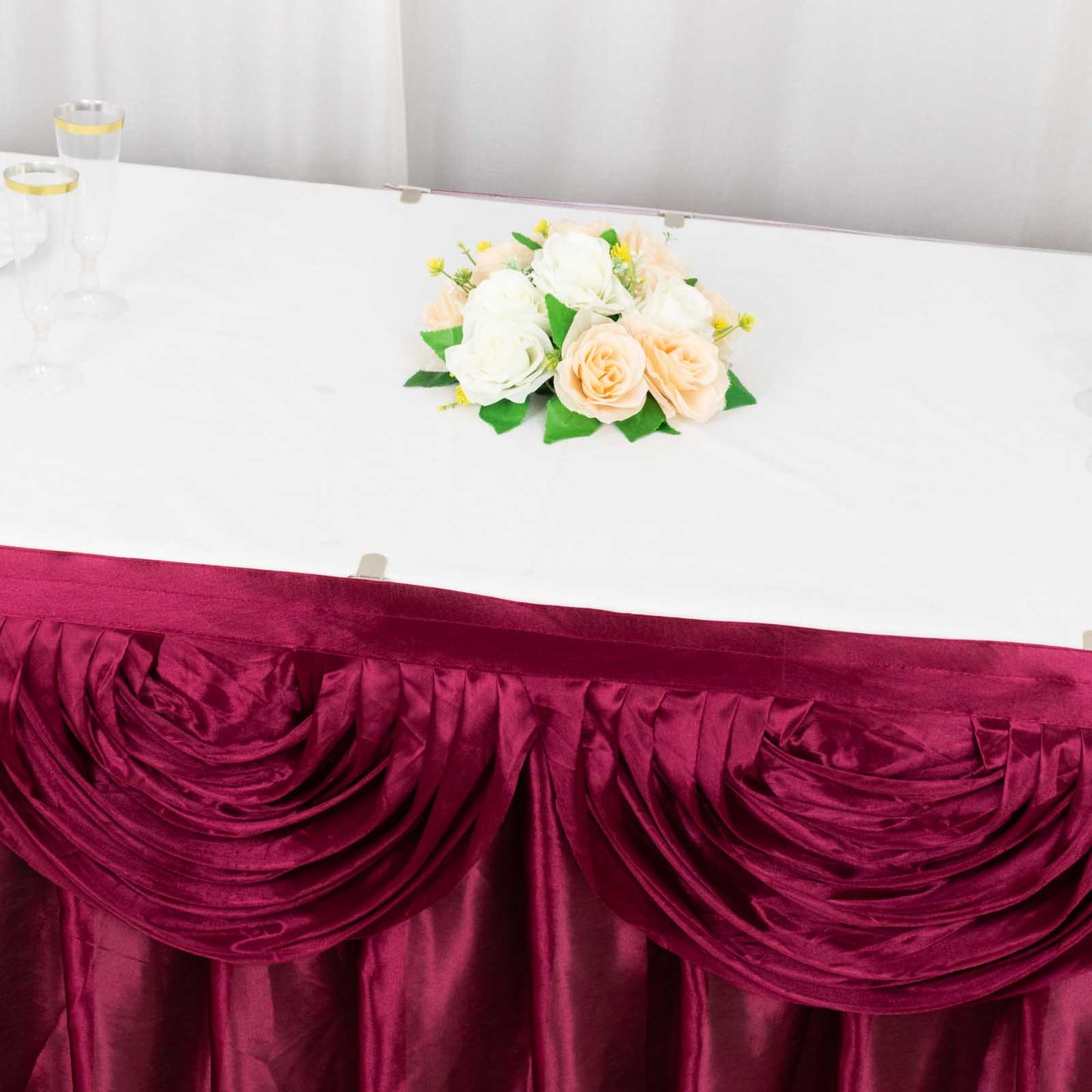 Burgundy pleated satin table skirt draping elegantly around a table.
