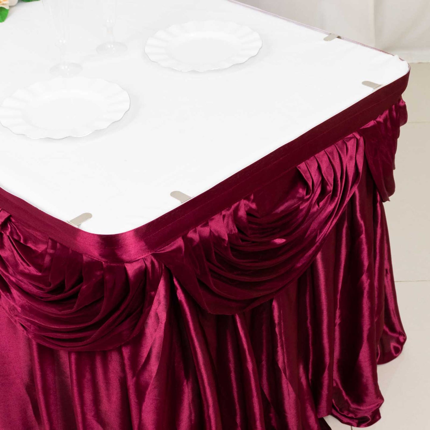 Burgundy pleated satin table skirt draped elegantly over a table.