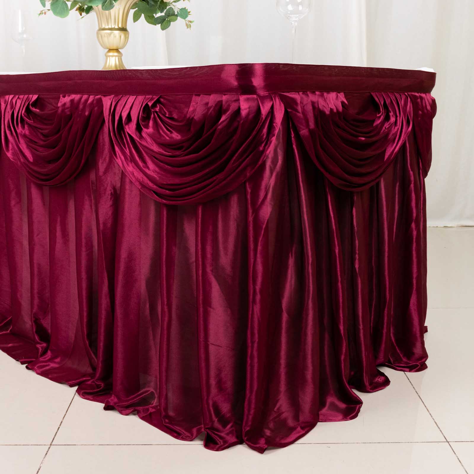 Burgundy pleated satin double drape table skirt on a table.