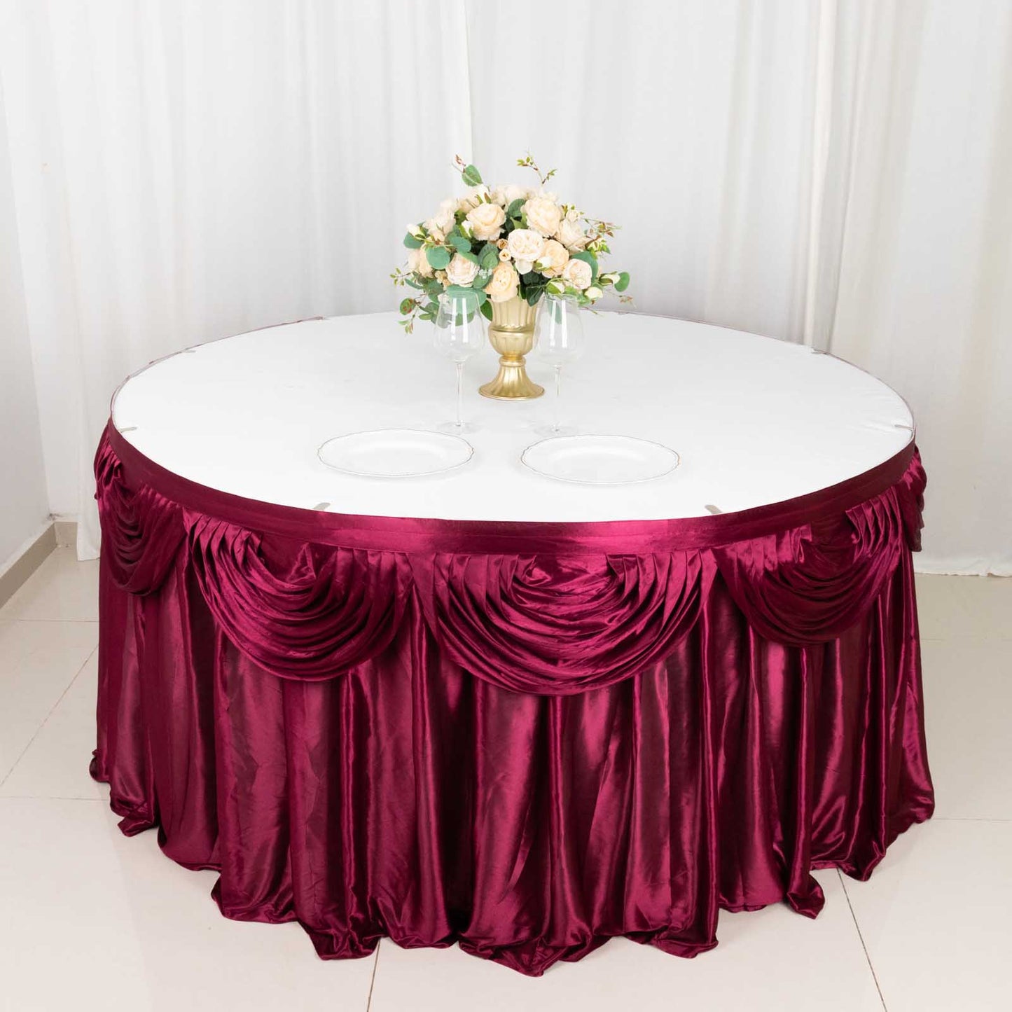 Burgundy pleated satin table skirt draping a round table with floral centerpiece.