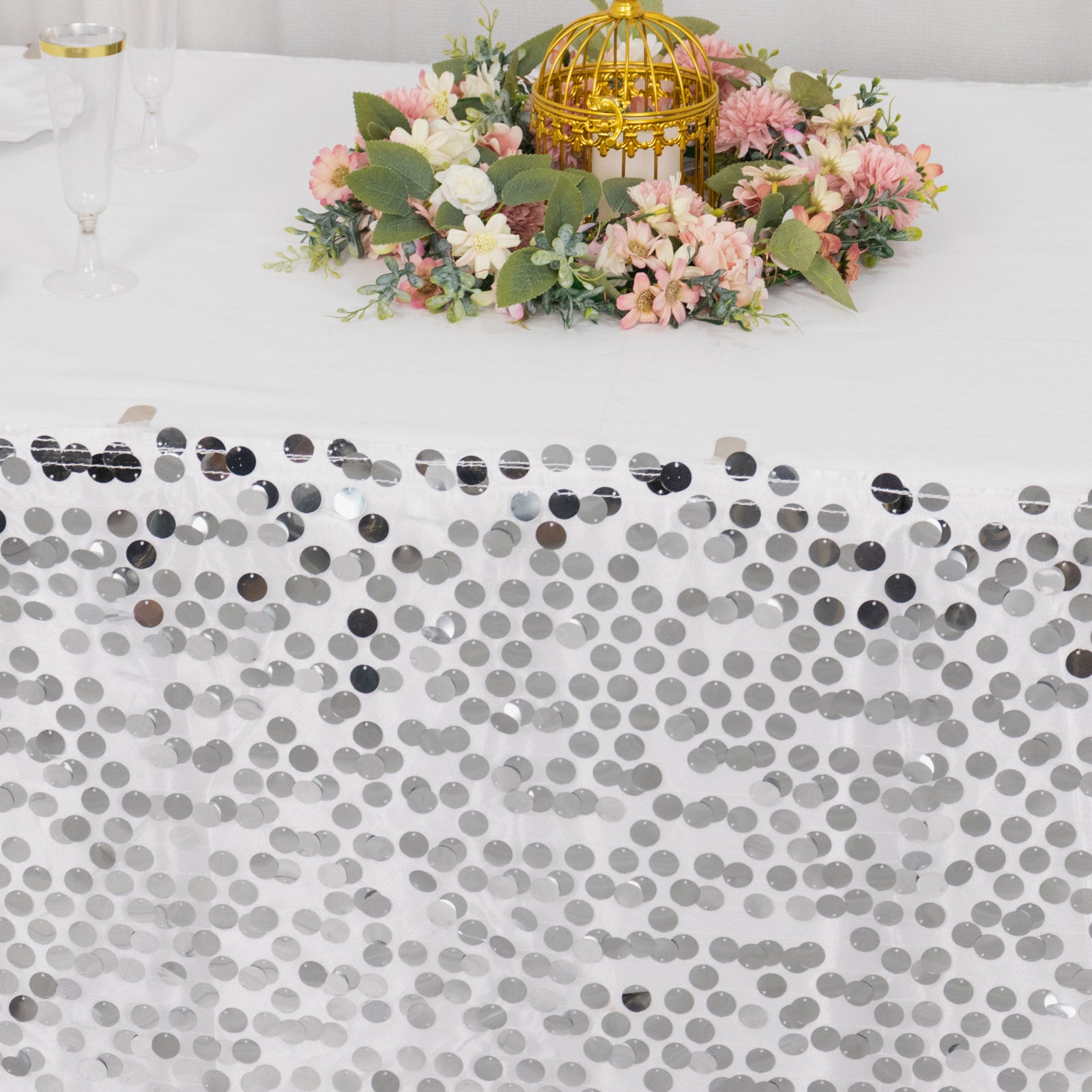Silver sequin table skirt with floral arrangement on a white table.