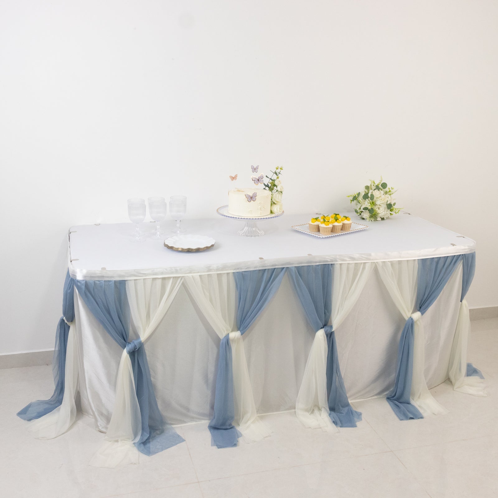 Dusty blue table decor with flowing drapes and a cake display on a white table.