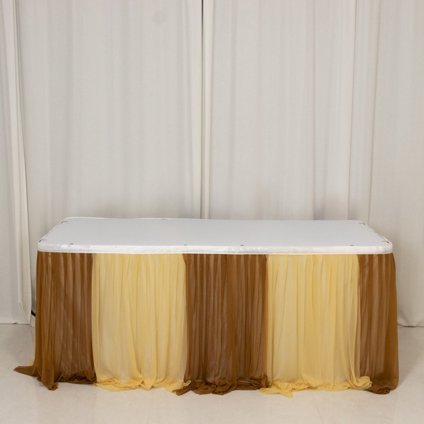 Gold table skirt with layered fabric drapes for elegant event decor.