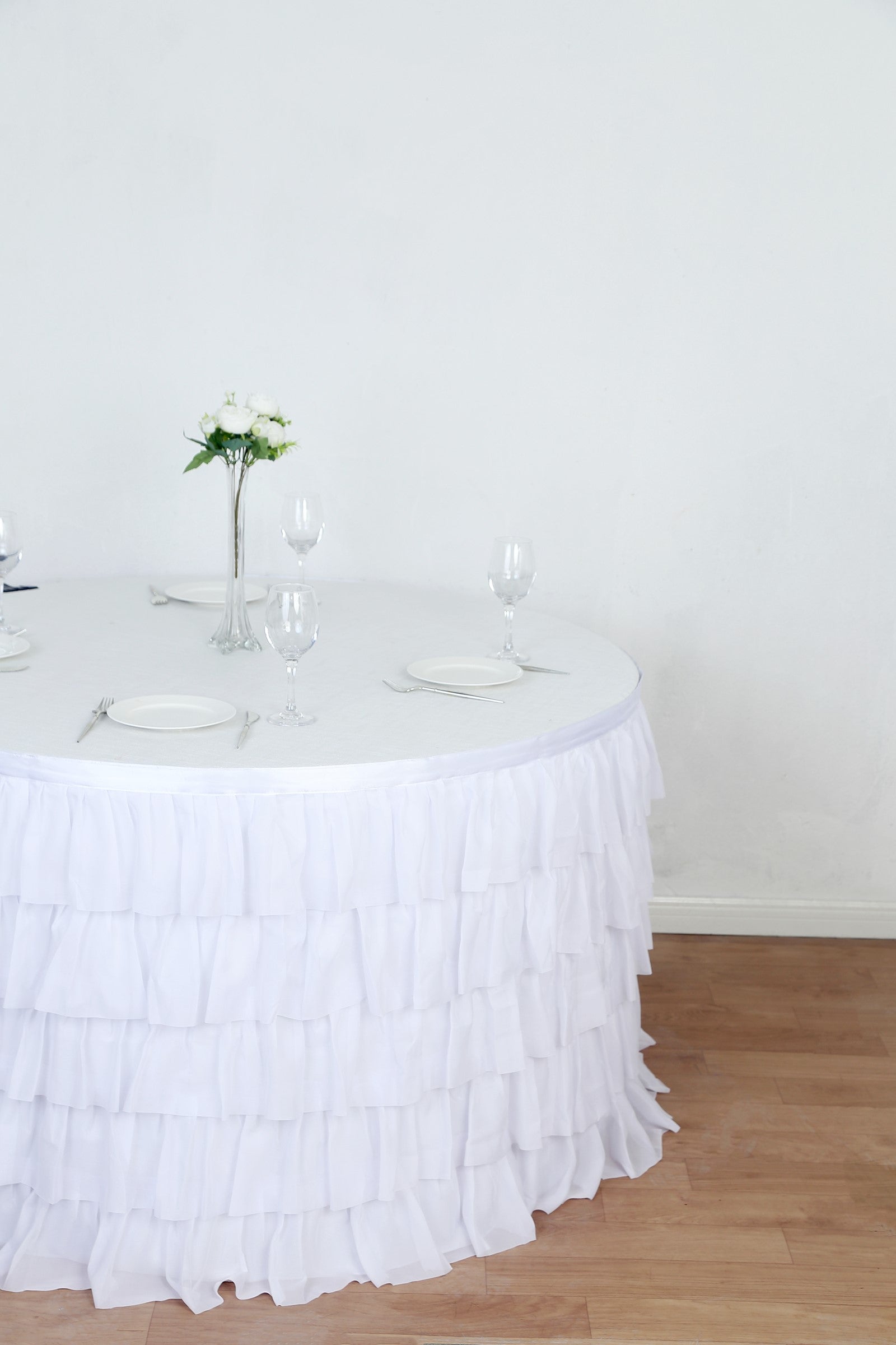 Elegant white ruffled tablecloth on a round table with floral centerpiece and glassware.