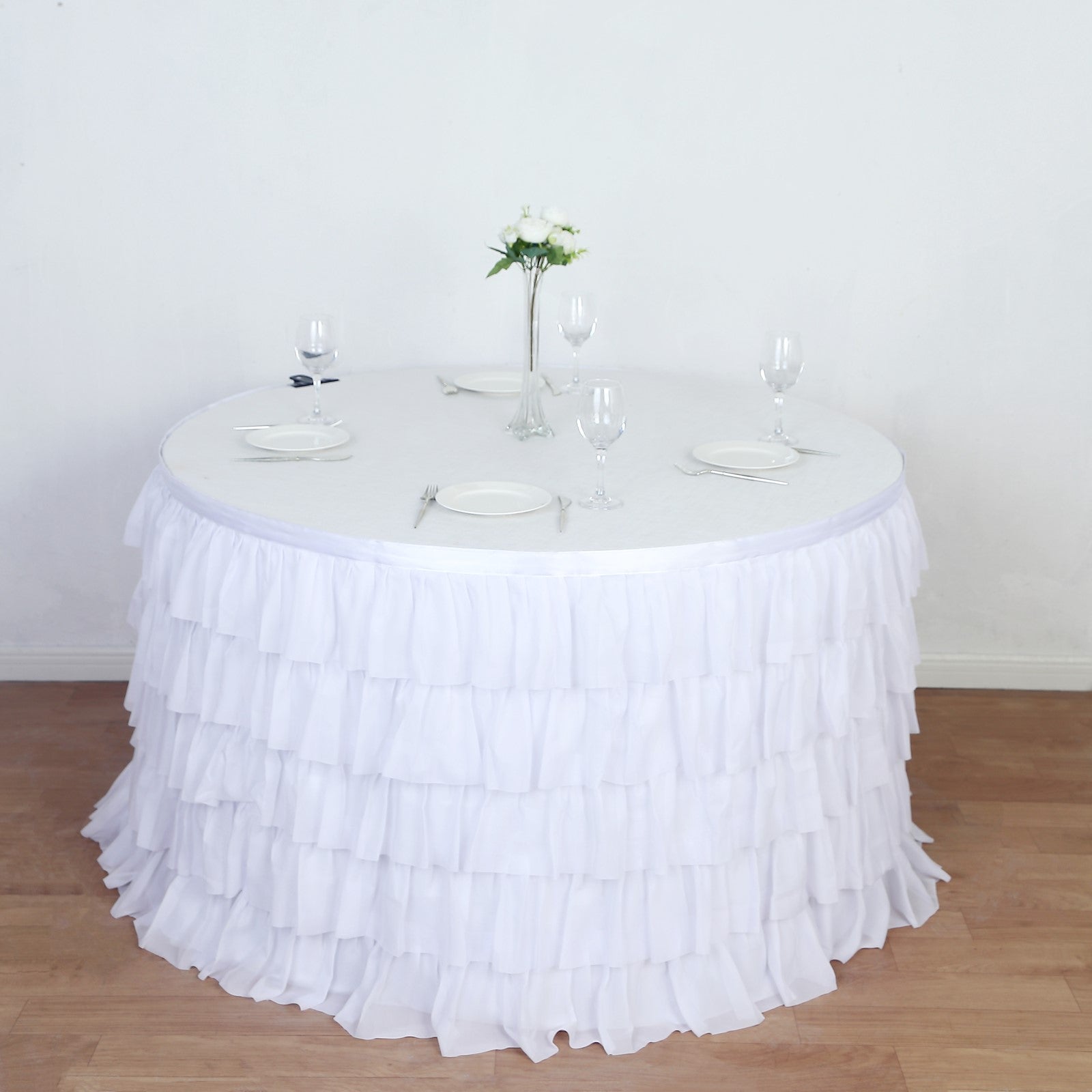 White ruffled tablecloth draping a round table set for an elegant dining experience.