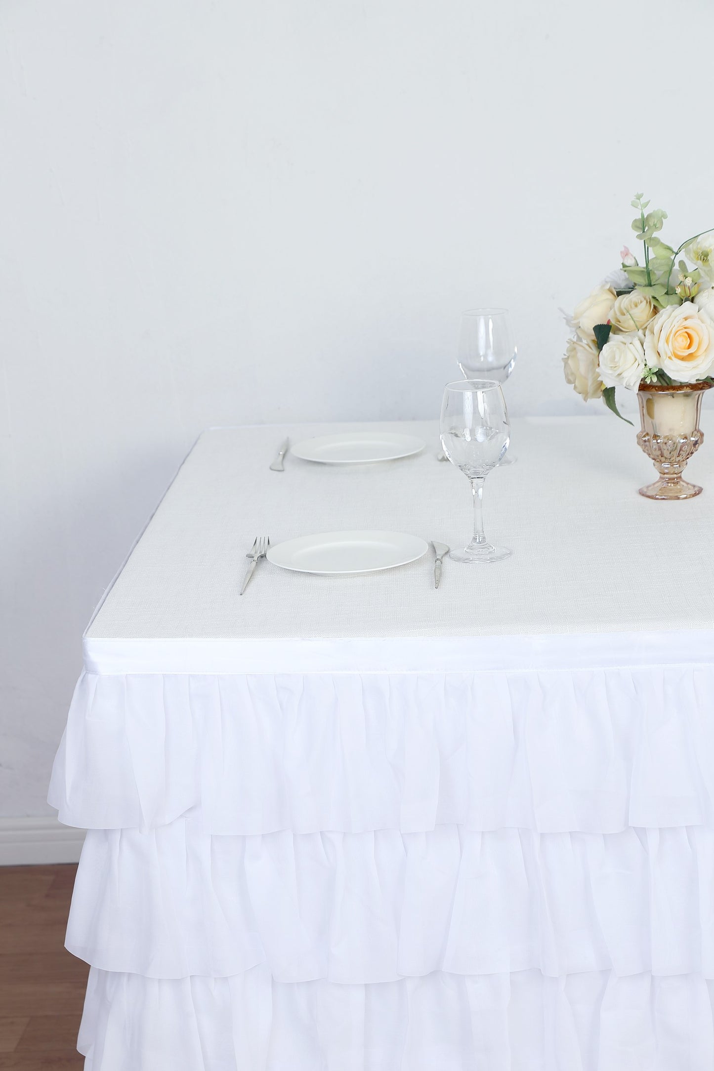 Elegant white table setting with ruffled tablecloth and floral centerpiece.