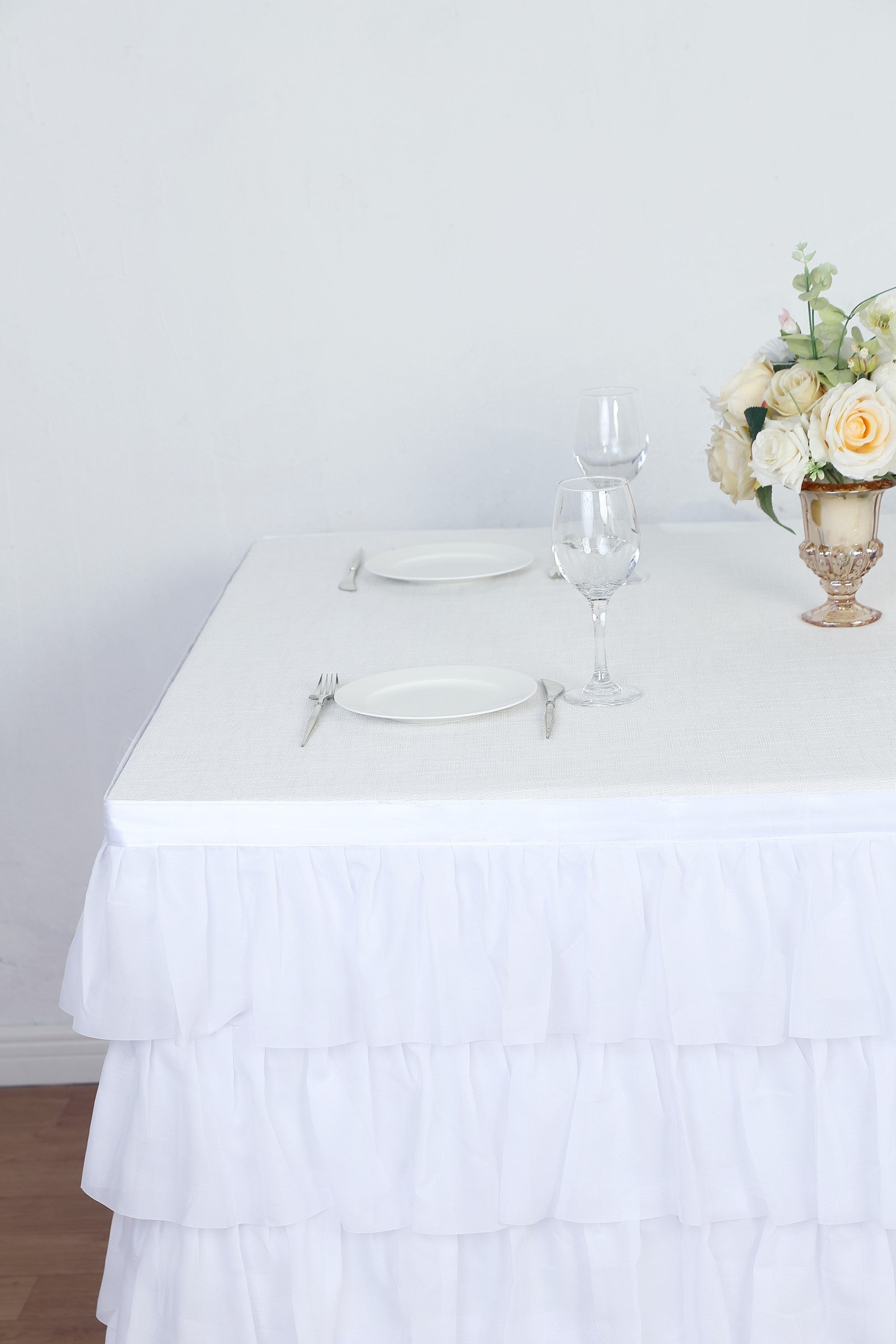 Elegant white table setting with ruffled tablecloth and floral centerpiece.