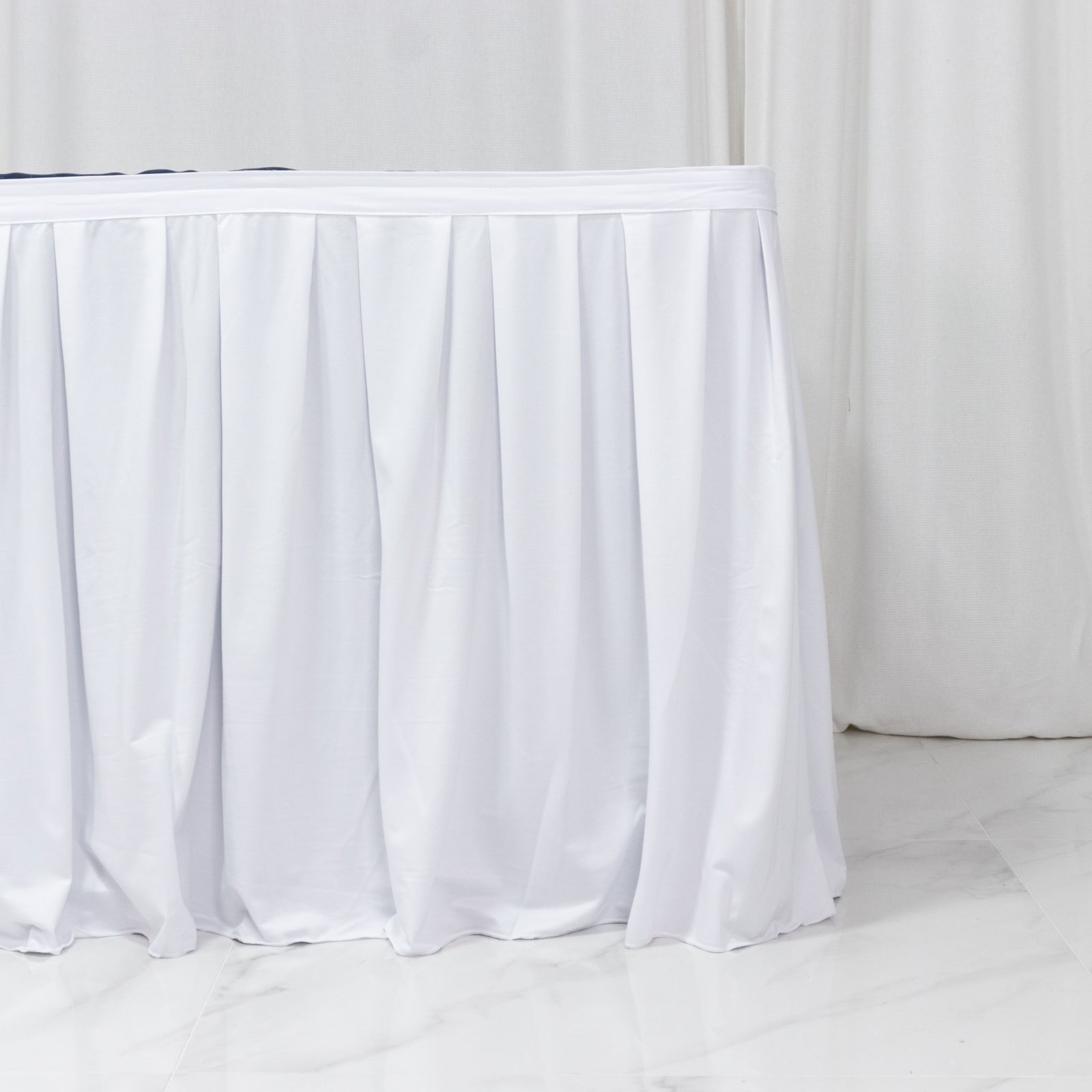 White pleated table skirt for events, wrinkle-free and stain-resistant.