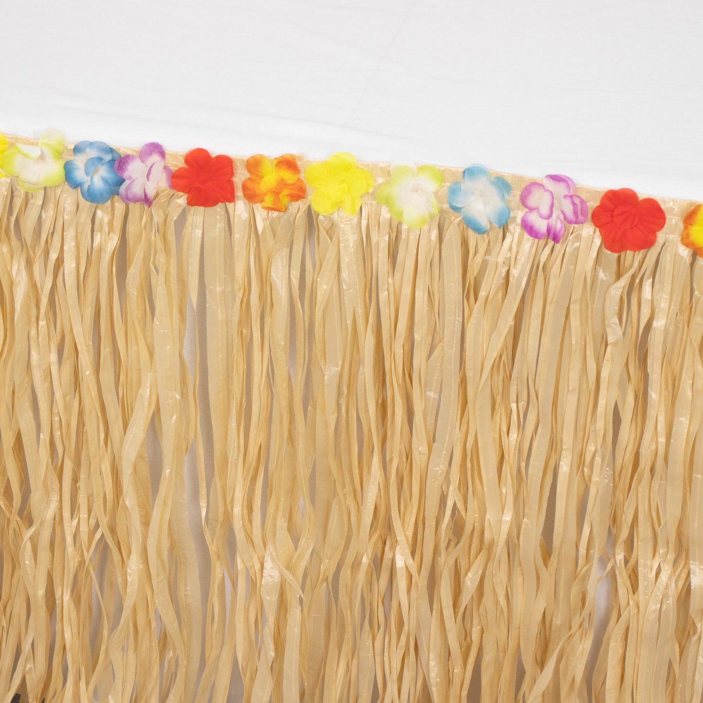Natural raffia grass table skirt with colorful flower accents for Hawaiian party.
