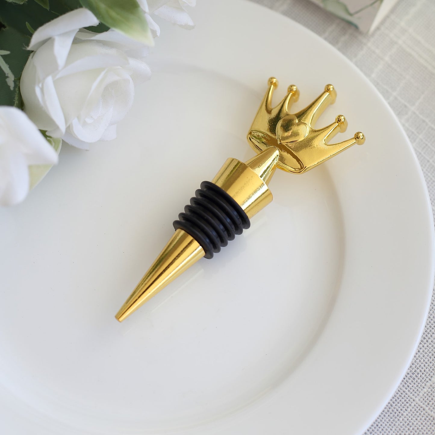 Gold princess crown wine bottle stopper with black rubber base on a white plate.