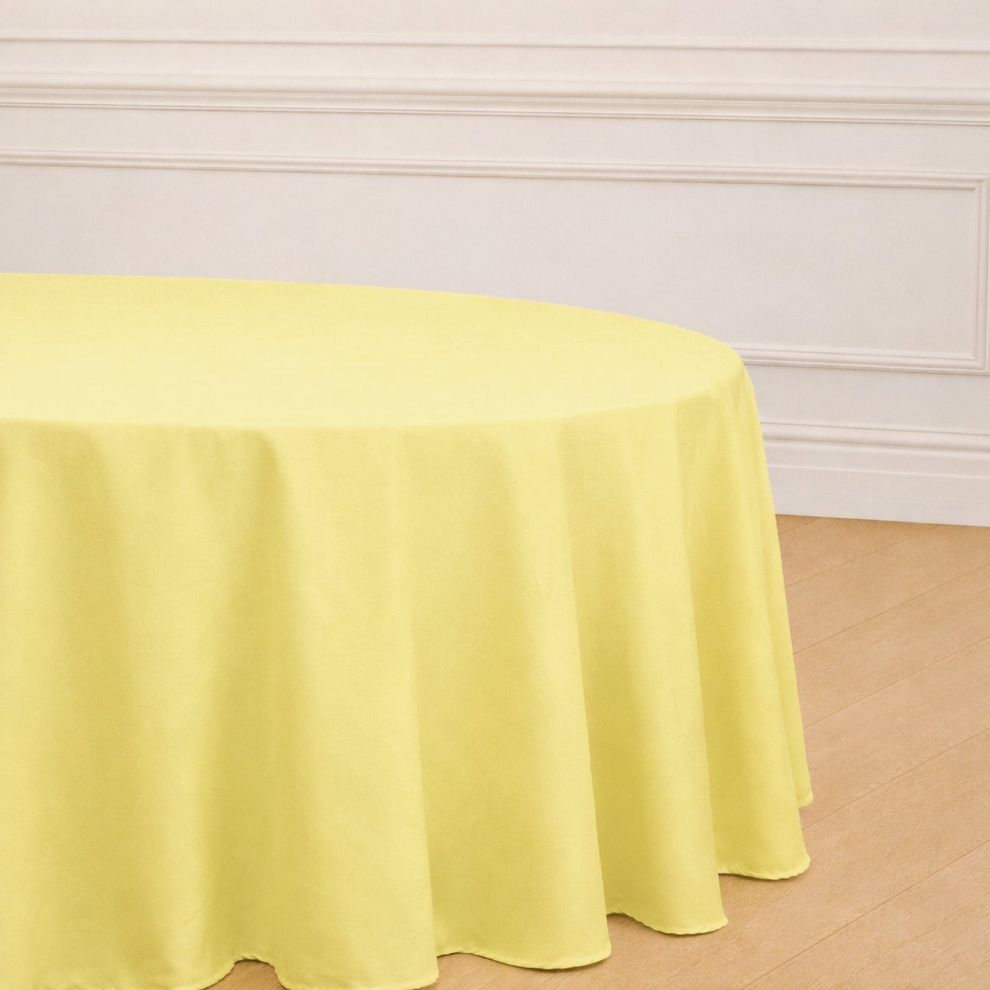 Yellow round polyester tablecloth on a wooden floor.