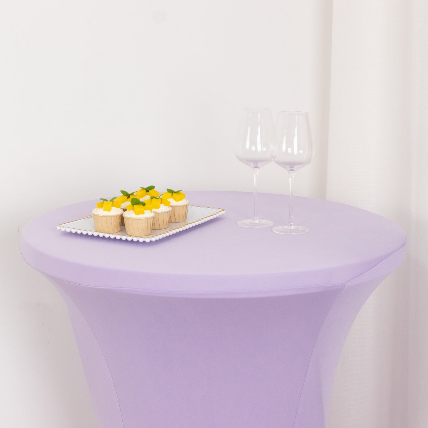 Lavender highboy spandex table cover with desserts and glasses on top.