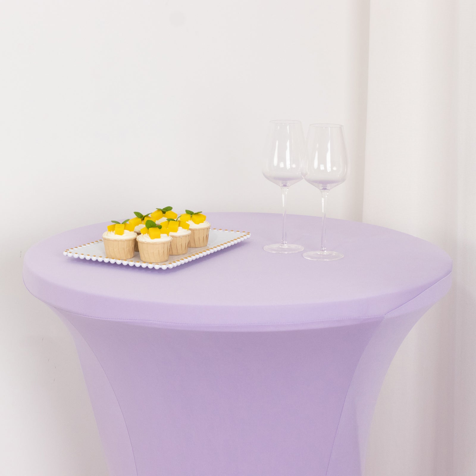 Lavender highboy spandex table cover with desserts and glasses on top.