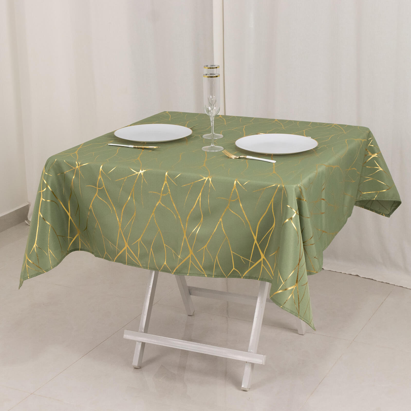 Dusty sage green tablecloth with gold foil tree branch pattern on a table.